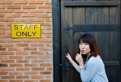 スペイン スタッフ専用の看板が掲げられた木製のドアにもたれかかるアジア系の若い女性。