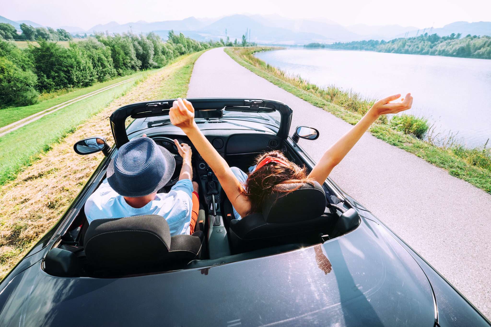 オープンカーに乗ったカップルが腕を上げて道路を走り、スペイン (スペイン) の美しい景色を楽しんでいます。