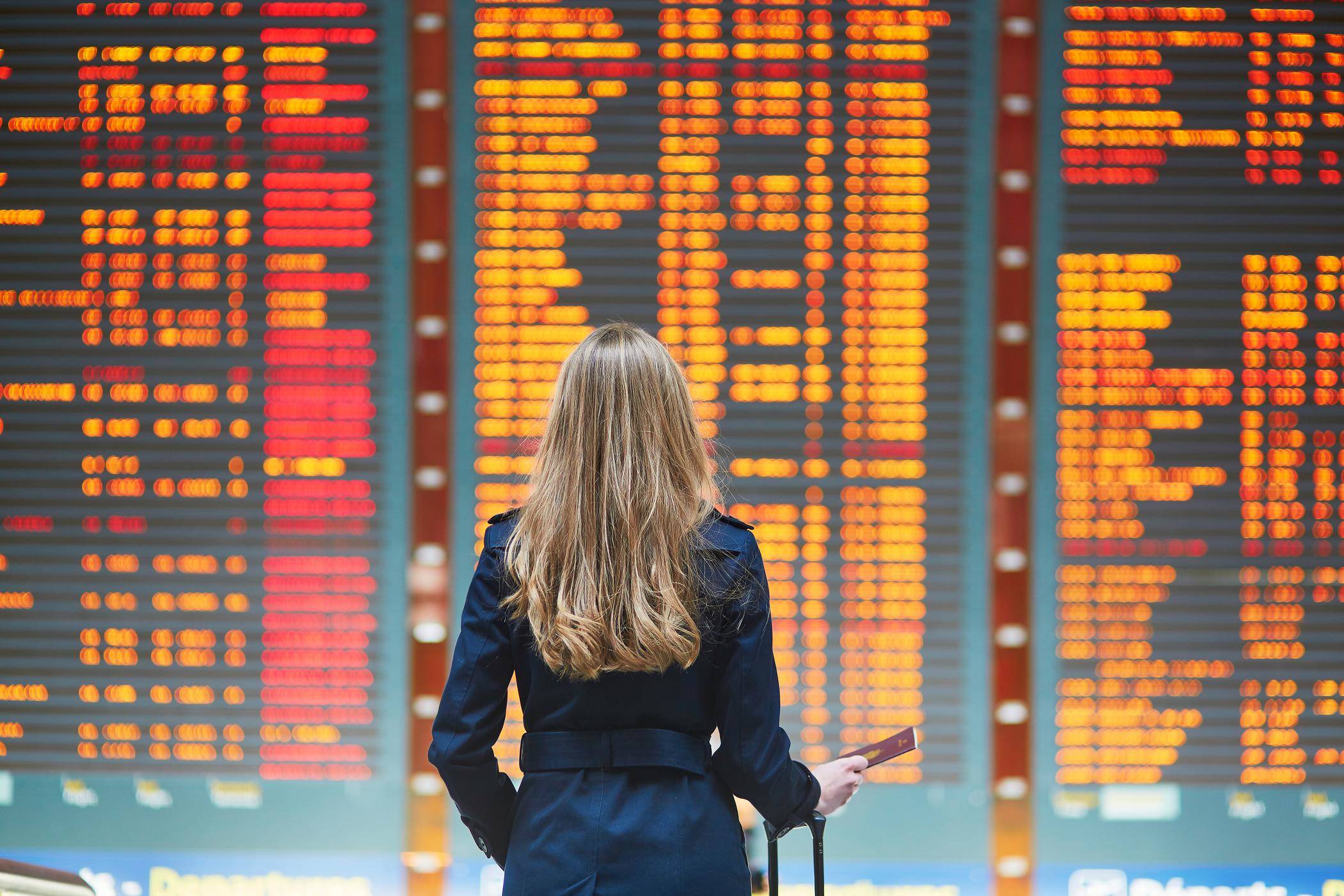 スペインから来た女性が空港の出発案内板の前に立っています。