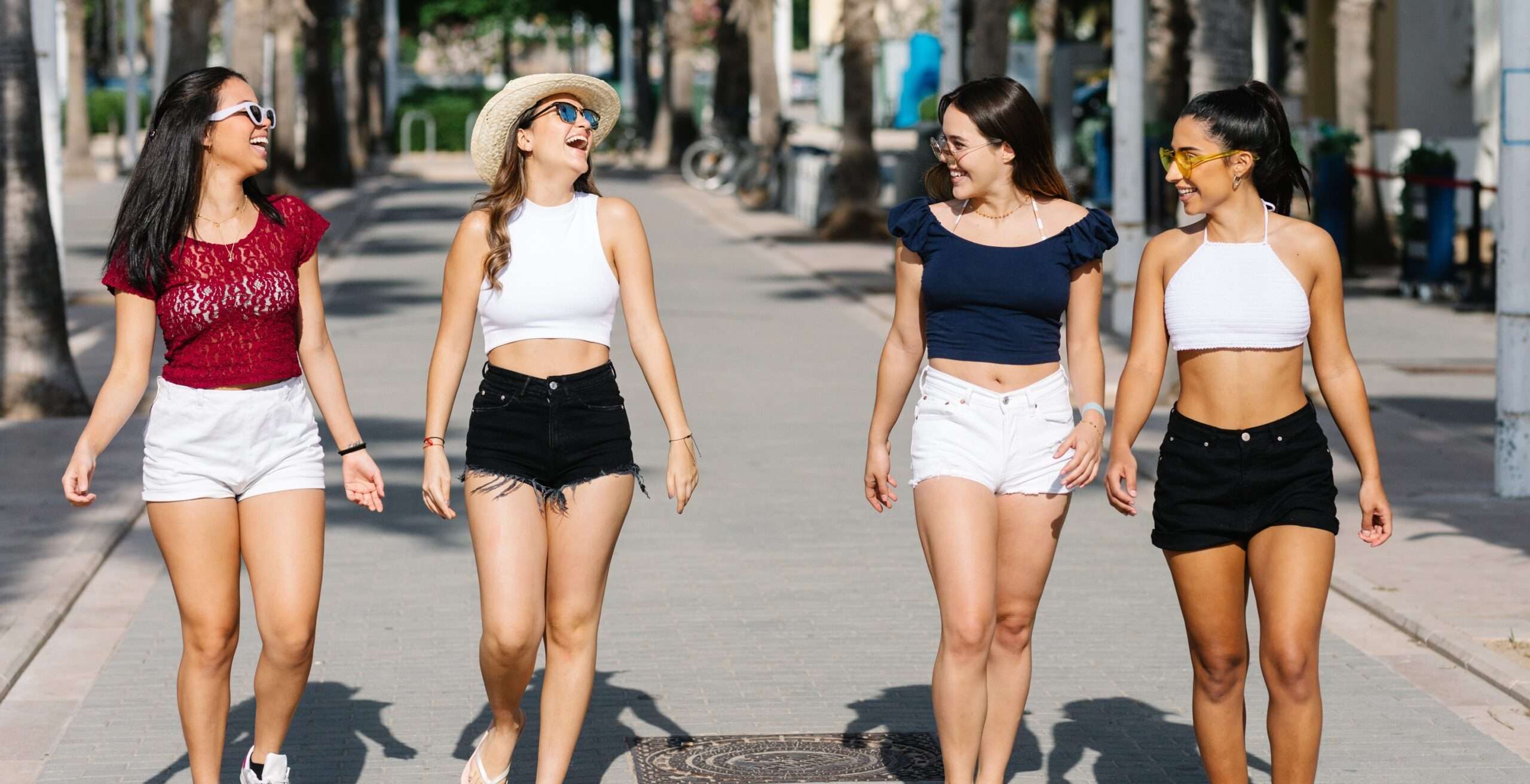 ショート パンツと帽子をかぶった 4 人の若い女性がスペインの通りを歩いています。
