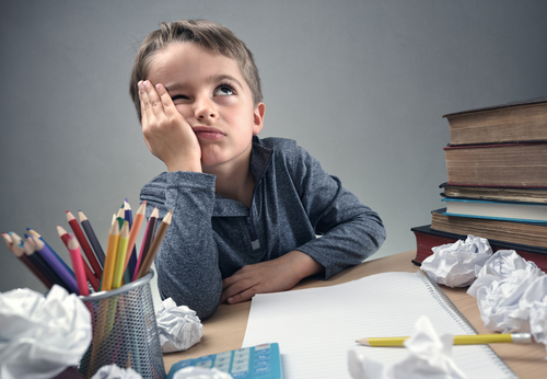 本や書類を持って机に座り、スペイン語を熱心に勉強している少年。