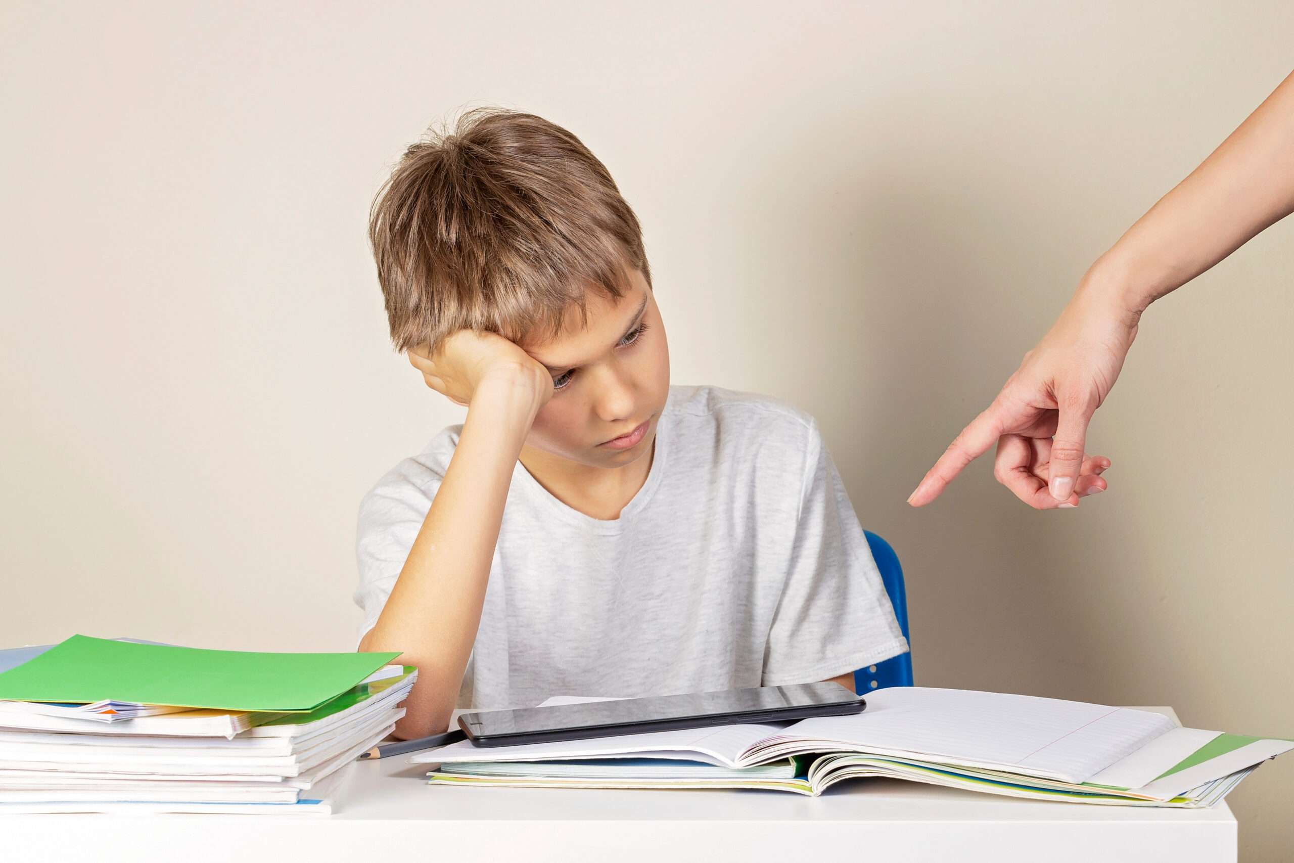 男の子が机に座り、スペイン語の表現で「デベル」を使いながら教師に指差されている。