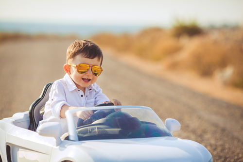 スペインの若い少年がサングラスをかけながらおもちゃの車を運転しています。