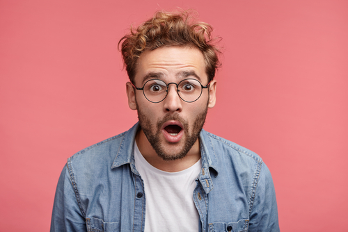 スペインのピンクの背景に眼鏡をかけた男性が驚いた表情をしている。