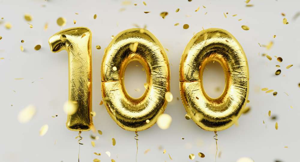 明るい背景に舞い降りる紙吹雪の中に金色の風船の数字が「100」を形成し、スペインの祝祭の祝祭精神を呼び起こします。