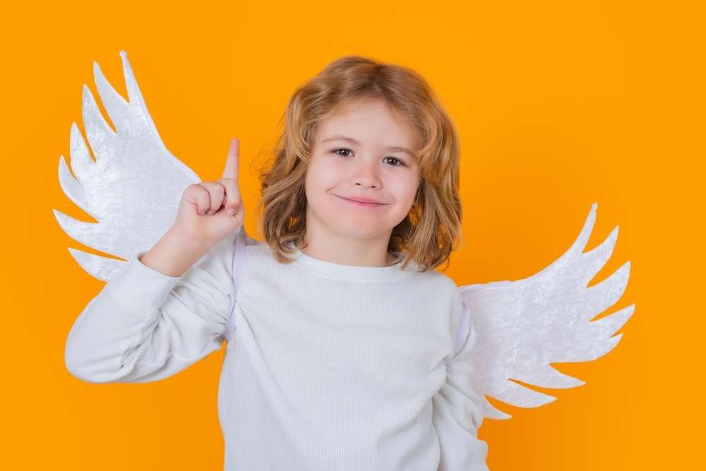 天使の羽と白い服を着た子供がオレンジ色の背景に指を立てており、スペインの古典芸術を彷彿とさせる穏やかな情景が浮かび上がります。