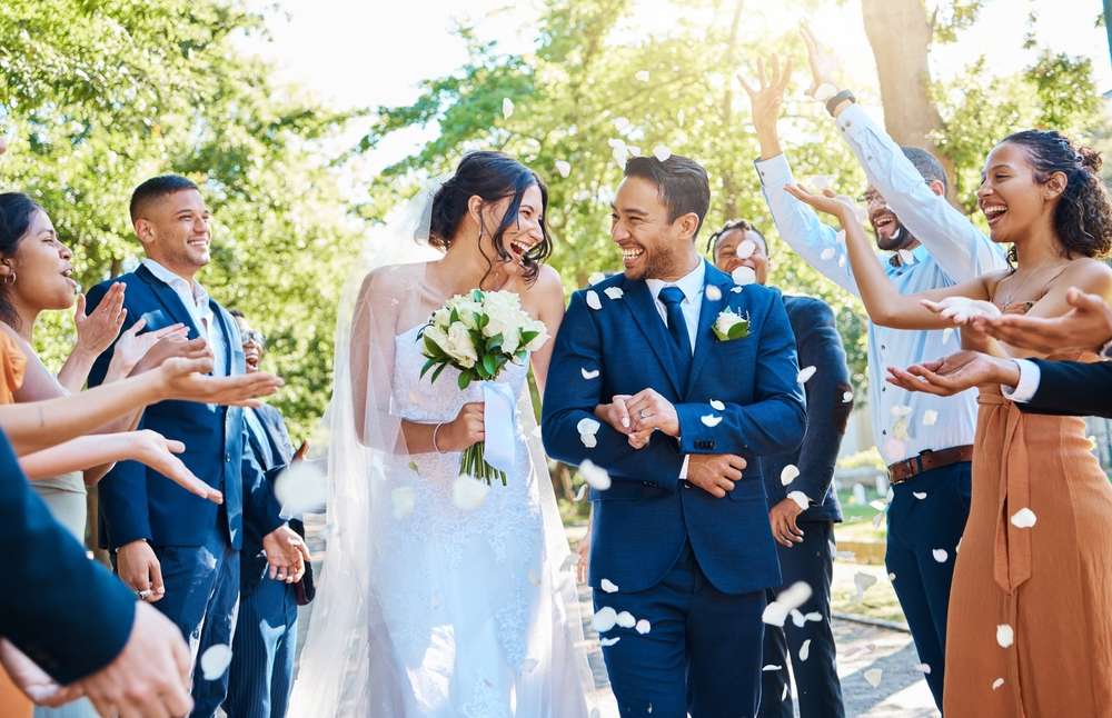 スペインをテーマにした美しい祝賀会で、花びらを投げる歓声を上げるゲストに囲まれながら、新郎新婦が笑顔で通路を歩いています。