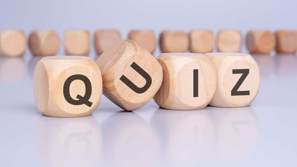 「QUIZ」と綴る「Q」、「U」、「I」、「Z」の文字が並んだ木製のブロックが前景にあり、木製のブロックがぼやけて背景に描かれています。これらの魅力的な教育ツールは、伝統的なスペインの職人技を彷彿とさせる素朴な優雅さを添えています。