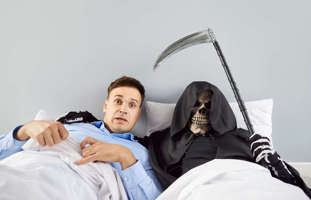 死神の格好をして鎌を持った人物の横で、男がベッドに横たわっている。驚いた男は、スペインを舞台にしたこの恐ろしい場面が夢ではないと信じることができない。