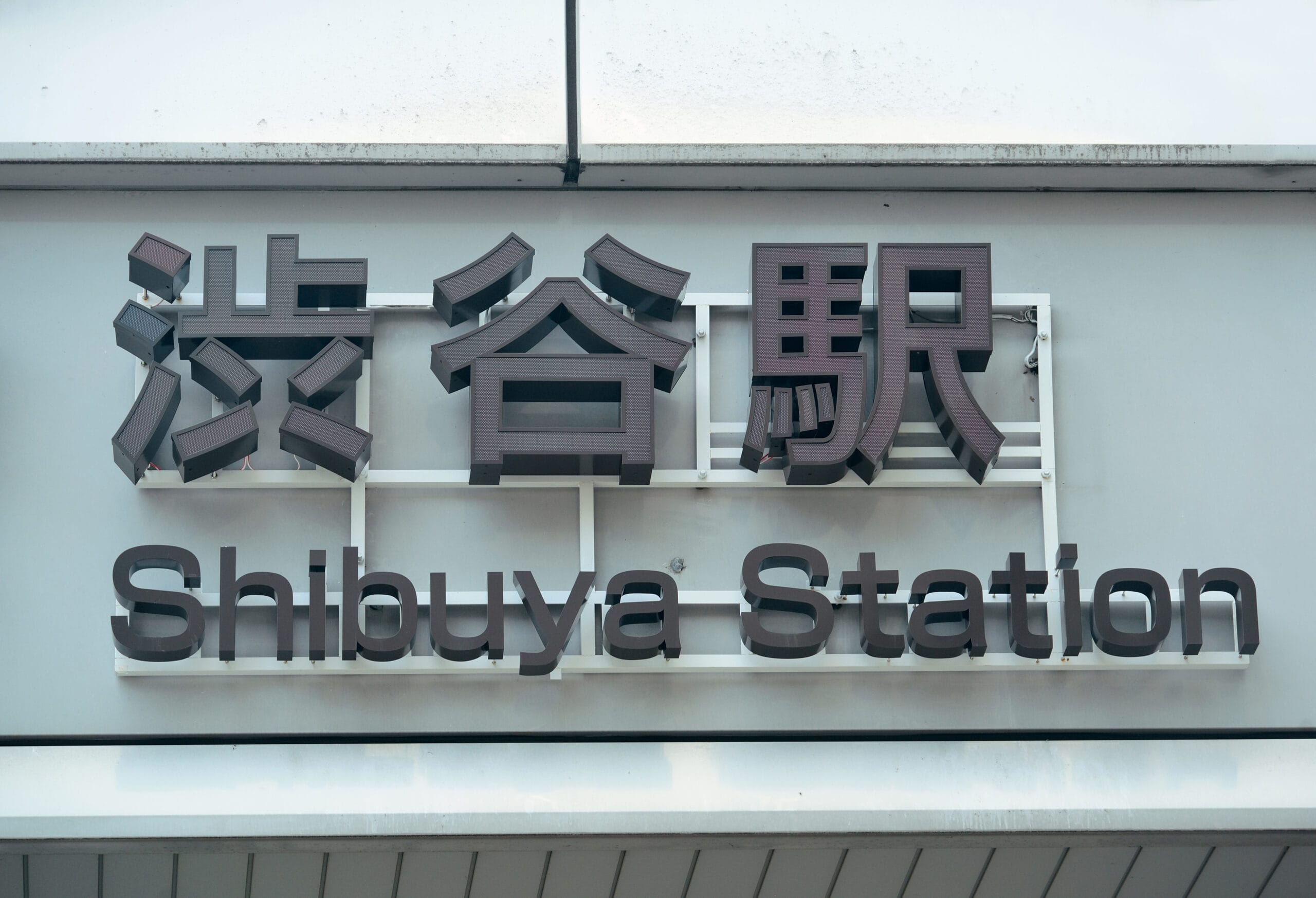スペイン語教室マンツーマンの近くの壁に貼られた、上に日本語、下に英語の「渋谷駅」の標識。.