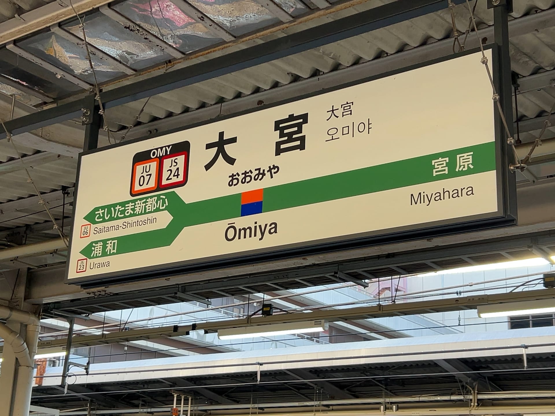 大宮駅の標識には漢字、ひらがな、ローマ字が表示されています。行き方としては、さいたま新都心、浦和、宮原などが挙げられます。近くには、個人に合わせた言語学習を提供するスペイン語教室マンツーマンがあります。.