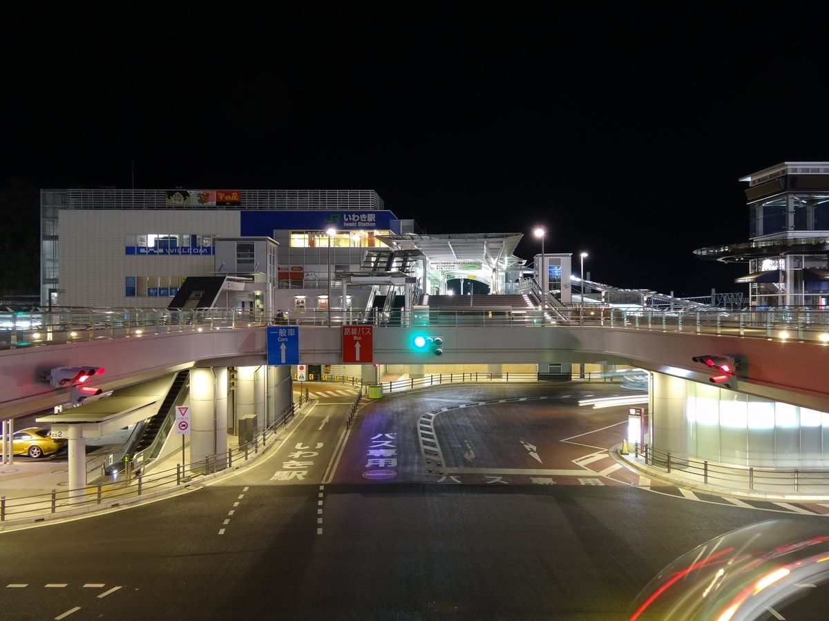 夜間の近代的な多層式駅。高架橋の下には、照明付きの看板や道路標示があり、交通量はほとんどない。.